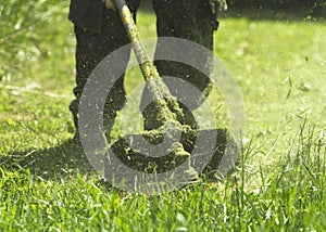 The man mowing green wild grass field using brush cutter mower or power tool string lawn trimmer