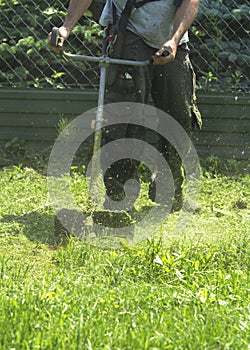 The man mowing green wild grass field using brush cutter mower or power tool string lawn trimmer