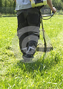 The man mowing green wild grass field using brush cutter mower or power tool string lawn trimmer