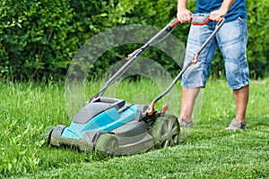 Man mowing the lawn with blue lawnmower in summertime