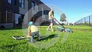 Man mowing lawn with lawn mower while son play with toy lawnmower. Gimbal