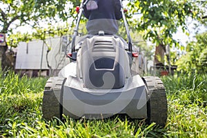 Man is mowing the lawn. Man with lawnmower is mowing green grass in the garden. Gardening