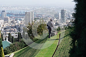 Man mowing a lawn using a lawnmower in Bahai Gardens on the Haifa panorama background