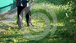 A man mows grass with a hand-held lawn mower outdoors. The gardener works in the yard.