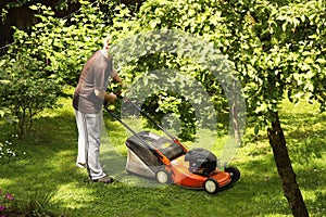 A man mows the grass with a lawnmower on the lawn of his garden. Care for English lawn. Landscape design country house. The