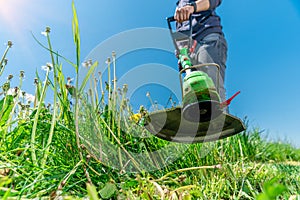 Man mows the grass in the meadow with a hand-held cordless lawnmower