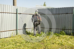 Man mows grass near fence. Man cuts lawn