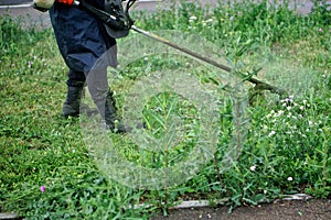 A man mows the grass and weeds on a city lawn using a hand-held lawn mower. Improvement and economy of a urban