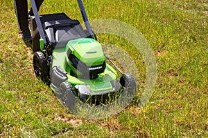 A man mows on green grass used by electric lawn mower