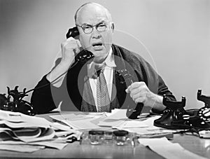 Man on multiple telephones looking angry