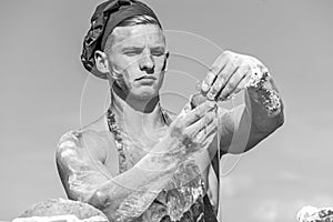 Man muscular baker or cook covered with flour working outdoor, sky on background. Baker adds egg to prepare dough