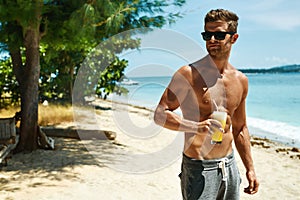 Man With Muscular Body Drinking Healthy Drink On Beach. Summer