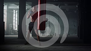 Man with muscular body punching bag in gym. Afro guy kicking sports bag