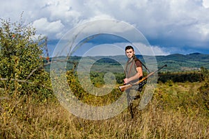 Man muscular brutal guy gamekeeper nature background. Hunter rifle gun stand top of mountain. Guy bearded hunter spend