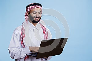 Man in muslim thobe texting on laptop photo