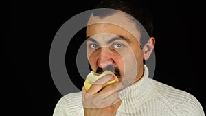 Man with mustache eating healthful green apple over black background