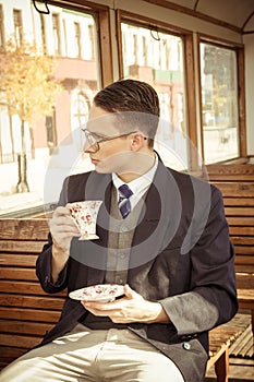 man with mustache and glasses on train wooden wagon drinking coffee or tea from cup and looking through window