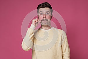 Man with mustache, making gesture with hand, zipping lips, promising to keep secret