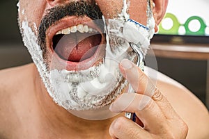 The man with the mustache is shaving and the man`s mouth is open