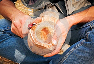 A man in nature carves a kuksa mug from wood. Handmade. Close-up