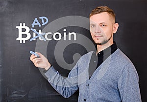 Man near a black school board on which is written bitkoin, part of the word Bitcoin is replaced by Bad photo