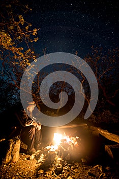 Man near the burning bonfire in the night under a starry sky