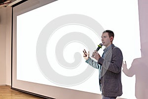 A man near the white screen of the projector with a micraphone talks about the project.