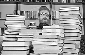 Man, nerd on surprised face between piles of books in library, bookshelves on background. Nerd concept. Teacher or