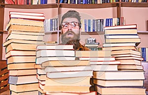 Man, nerd on surprised face between piles of books in library, bookshelves on background. Nerd concept. Teacher or