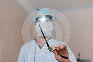 Man neurosurgeon in glasses with binary loupes for microsurgery shows a black clamp. Modern medicine. Medical instruments. photo