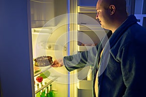 Man at night overstep and take whole chocolate cake from refrige