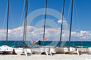 Man with oars goes on sea front. A lot of catamarans stay on the