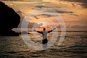 Man on ocean enjoying sunset on Bali with arms wide open