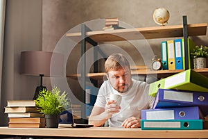 A man in the office behind a stack of folders and a laptop. Abused at work, making decisions at work. Male freelancer at home work