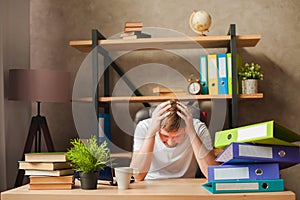 A man in the office behind a stack of folders and a laptop. Abused at work, making decisions at work. Male freelancer at home work