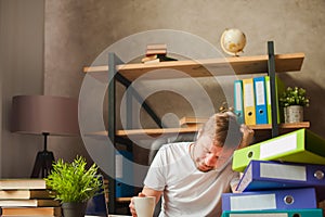 A man in the office behind a stack of folders and a laptop. Abused at work, making decisions at work. Male freelancer at home work