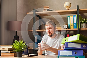 A man in the office behind a stack of folders and a laptop. Abused at work, making decisions at work. Male freelancer at home work