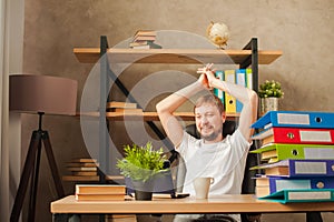 A man in the office behind a stack of folders and a laptop. Abused at work, making decisions at work. Male freelancer at home work