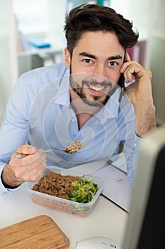 man in office eating salad while on phone