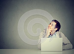 Man in office, sitting at desk with laptop daydreaming, smiling