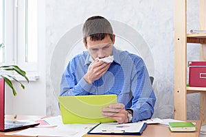 A man in the office with a tablet in his hand coughs in a napkin