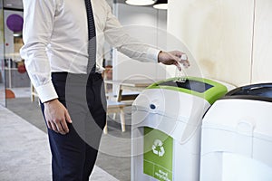 Man in an office throwing plastic bottle into recycling bin