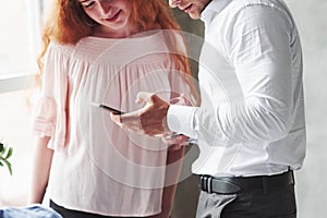 Man in office wear showing information on his phone to a readhead girl