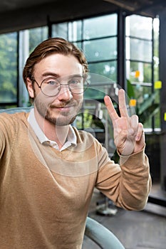 Man in office wearing shirt and glasses smiling and looking at smartphone camera, businessman taking selfie and talking