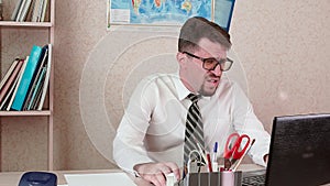 A man is an office worker with a beard and glasses working at a laptop