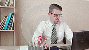 A man is an office worker with a beard and glasses working at a laptop