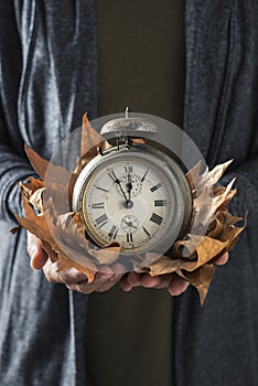 Man with old alarm clock and dry leaves