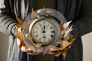 Man with old alarm clock and dry leaves