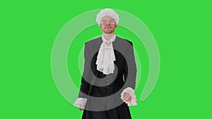 Man in old-fashioned laced frock coat and white wig walking in a mannered way looking at camera on a Green Screen