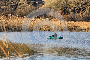 A man in an old inflatable boat is fishing in the lake with a fishing rod, but against the background of yellow reeds